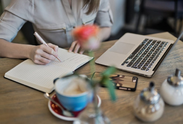 A female student focuses on her assignment, typing on her laptop and jotting down notes in her diary.